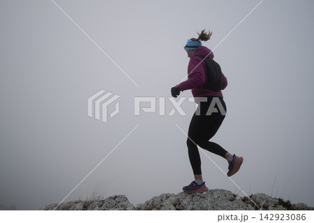 Trail Runner Woman Jogging on Foggy Rock Ridge in Winter Running Gear for Fitness 142923086