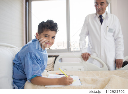 Smiling boy drawing in hospital bed during consultation with doctor at eye clinic in Egypt 142923702