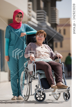 Middle Eastern nurse with patient in wheelchair outside eye hospital clinic in Egypt providing compassionate healthcare support Middle Eastern nurse with patient in wheelchair outside eye hospital clinic in Egypt providing compassionate healthcare support 142923839