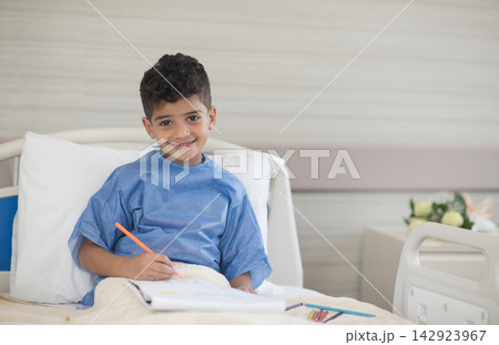 Smiling Middle Eastern boy patient in a modern Egyptian eye hospital clinic bed drawing during recovery Smiling Middle Eastern boy patient in a modern Egyptian eye hospital clinic bed drawing during recovery 142923967