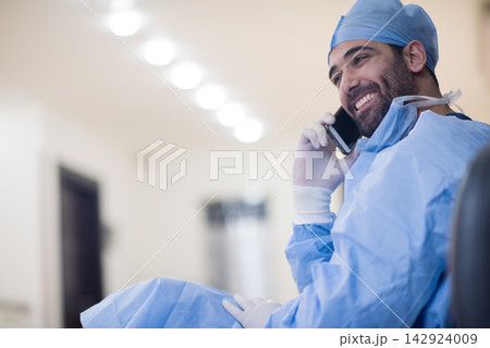 Smiling Middle Eastern eye surgeon in scrubs talking on phone at a small clinic in Egypt Smiling Middle Eastern eye surgeon in scrubs talking on phone at a small clinic in Egypt 142924009