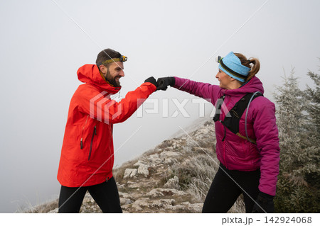 Couple Fist Bumping on Foggy Mountain Hike During Winter Adventure With Headlamps and Warm Jackets 142924068