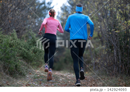 Couple Trail Running Together Through Forest Pathway During Outdoor Fitness Jogging Session Couple Trail Running Together Through Forest Pathway During Outdoor Fitness Jogging Session 142924093