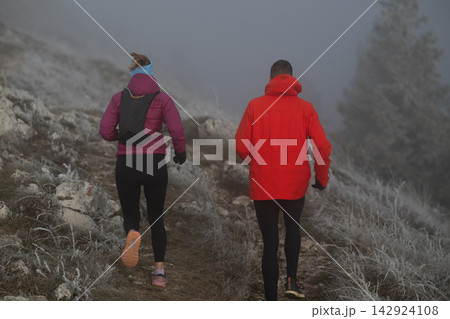 Couple Trail Running Through Foggy Frosty Mountain Path During Winter Outdoor Workout 142924108
