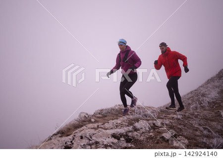 Couple Trail Running On Foggy Mountain Ridge In Winter Wearing Headlamps And Cold-Weather Gear 142924140