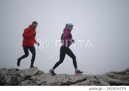 Trail Runners With Headlamps Running Along Foggy Rocky Ridge in Cold Weather Outdoor Training Trail Runners With Headlamps Running Along Foggy Rocky Ridge in Cold Weather Outdoor Training 142924259