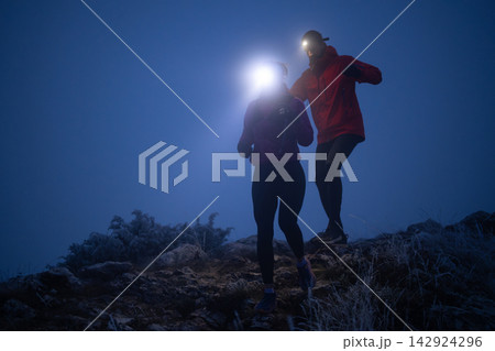 Night Trail Running Couple With Headlamps On Foggy Mountain Path Showing Teamwork And Adventure Night Trail Running Couple With Headlamps On Foggy Mountain Path Showing Teamwork And Adventure 142924296