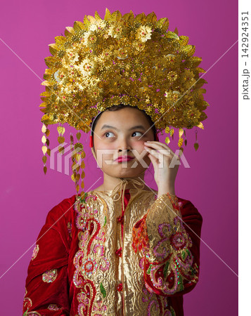 Young Indonesian Asian Girl Wearing Traditional Gold Headdress and Embroidered Red Dress Portrait for Cultural Festival Young Indonesian Asian Girl Wearing Traditional Gold Headdress and Embroidered Red Dress Portrait for Cultural Festival 142924351