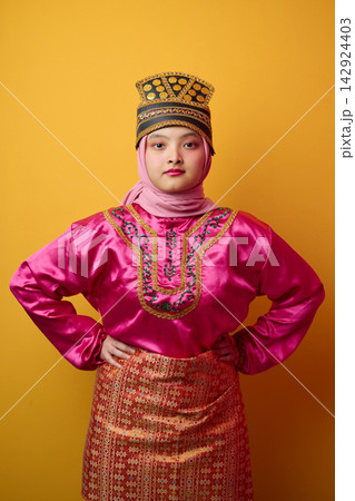 Confident Young Indonesian Asian Woman in Traditional Malay Costume and Hijab Wearing Ornate Headdress on Yellow Background Confident Young Indonesian Asian Woman in Traditional Malay Costume and Hijab Wearing Ornate Headdress on Yellow Background 142924403