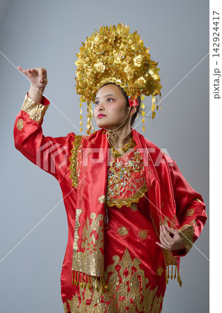 Indonesian Asian Woman Wearing Ornate Gold Headdress and Red Traditional Ceremonial Costume Posing Gracefully Indonesian Asian Woman Wearing Ornate Gold Headdress and Red Traditional Ceremonial Costume Posing Gracefully 142924417