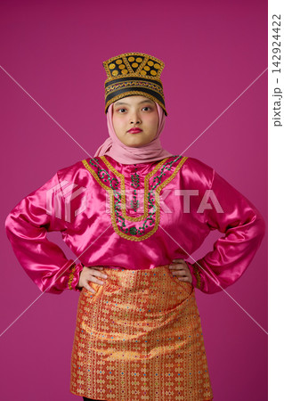 Confident Indonesian Asian Woman in Bright Pink Traditional Costume and Hijab Wearing Ornate Gold Headdress Confident Indonesian Asian Woman in Bright Pink Traditional Costume and Hijab Wearing Ornate Gold Headdress 142924422