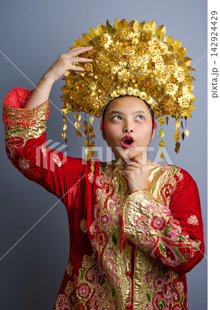 Young Indonesian Asian Girl Wearing Gold Headdress and Red Traditional Costume Expressing Surprise Young Indonesian Asian Girl Wearing Gold Headdress and Red Traditional Costume Expressing Surprise 142924429