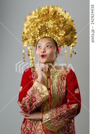 Young Indonesian Asian Girl in Gold Floral Headdress and Embroidered Red Traditional Costume Looking Surprised Young Indonesian Asian Girl in Gold Floral Headdress and Embroidered Red Traditional Costume Looking Surprised 142924438