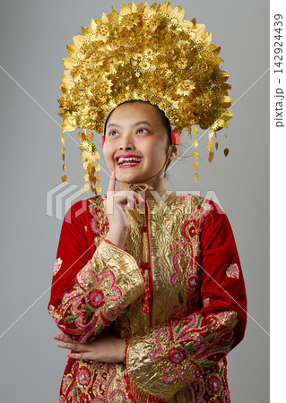 Young Indonesian Asian Girl Portrait Wearing Ornate Gold Headdress and Red Traditional Costume Celebrating Cultural Heritage Young Indonesian Asian Girl Portrait Wearing Ornate Gold Headdress and Red Traditional Costume Celebrating Cultural Heritage 142924439