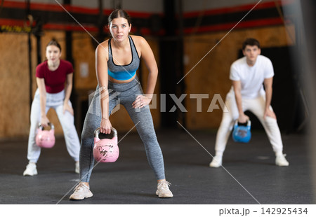 Girl in gym does exercises with kettlebell, lifts and lowers heavy kettlebell with one hand Girl in gym does exercises with kettlebell, lifts and lowers heavy kettlebell with one hand 142925434