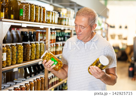Elderly man choosing pickled olives in jars in grocery store 142925715