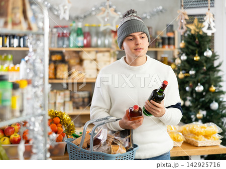 Young man examines alcohol whisky bottle in store. Young man examines alcohol whisky bottle in store. 142925716