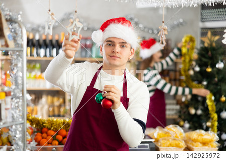 Young guy seller decorates grocery store for christmas Young guy seller decorates grocery store for christmas 142925972