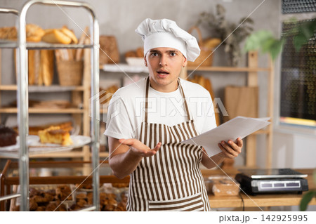 Frustrated male owner of bakery reads documents and reflects, makes decisions. 142925995