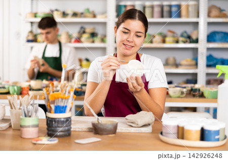 Woman painting with brush on handmade clay cup Woman painting with brush on handmade clay cup 142926248