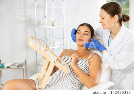 Adult female cosmetologist examining face of female patient Adult female cosmetologist examining face of female patient 142926359