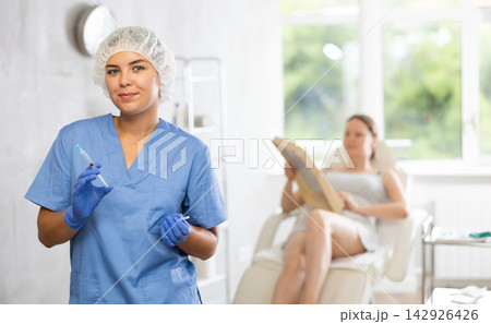 Nurse in disposable cap with syringe in hand and conducts preparatory activities before injections. 142926426