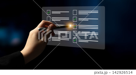 Hand with pen marking checklist items on transparent digital screen with glowing checkmarks, symbolizing task completion and productivity in modern work environment Cyphers. 142926514
