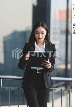 Business woman checks phone in front of modern building during the day 142927594