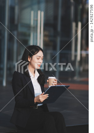 Young brunette business lady dressed in black jacket checking work chats sitting outside with laptop Young brunette business lady dressed in black jacket checking work chats sitting outside with laptop 142927596