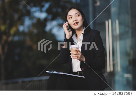 Young brunette business lady dressed in black jacket checking work chats sitting outside with laptop 142927597