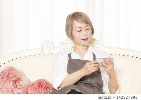 リビングでスマホを使いこなすシニア女性 142927998