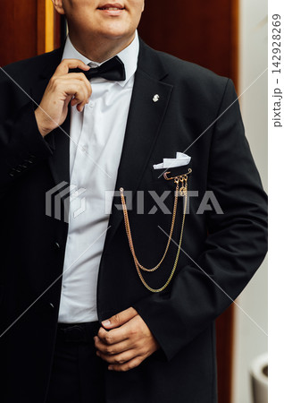 Groom in elegant black suit and bow tie with luxury gold chain brooch. Groom in elegant black suit and bow tie with luxury gold chain brooch. 142928269