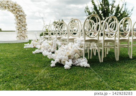 Wedding arch decorated with flowers and lights and white chairs for guests. Wedding ceremony. 142928283