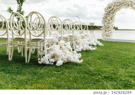 Wedding arch decorated with flowers and lights and white chairs for guests. Wedding ceremony. Wedding arch decorated with flowers and lights and white chairs for guests. Wedding ceremony. 142928284