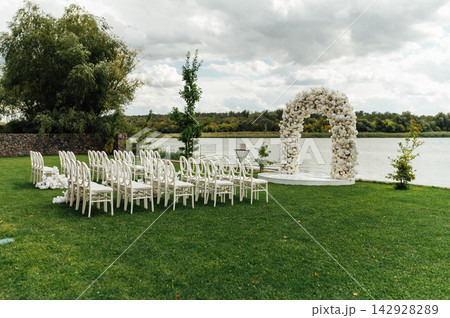 Wedding arch decorated with flowers and lights and white chairs for guests. Wedding ceremony. Wedding arch decorated with flowers and lights and white chairs for guests. Wedding ceremony. 142928289