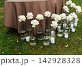 Modern wedding floor decor with white roses in glass vases and candles on grass lawn. 142928328