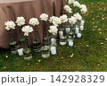 Modern wedding floor decor with white roses in glass vases and candles on grass lawn. 142928329