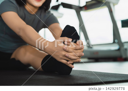 Close-up of woman stretching leg seated on exercise mat in gym preparing for workout or cool down routine Close-up of woman stretching leg seated on exercise mat in gym preparing for workout or cool down routine 142929778