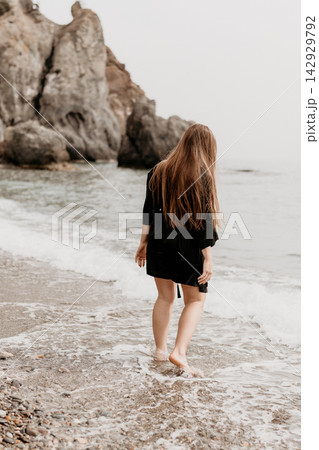 Woman beach ocean walking barefoot on a rocky shore toward waves with massive cliffs in the misty background Woman beach ocean walking barefoot on a rocky shore toward waves with massive cliffs in the misty background 142929792