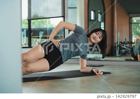 Young woman wearing workout clothes doing side plank exercise on yoga mat indoors in modern gym with natural light Young woman wearing workout clothes doing side plank exercise on yoga mat indoors in modern gym with natural light 142929797