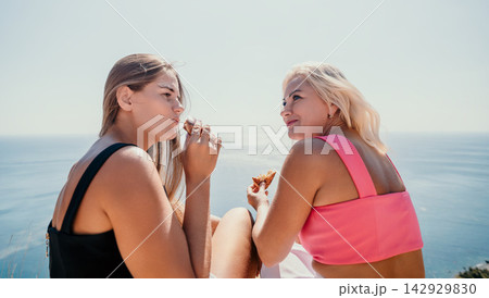 Women picnic coast sitting on a cliff and eating snacks with beautiful ocean view during summer vacation Women picnic coast sitting on a cliff and eating snacks with beautiful ocean view during summer vacation 142929830