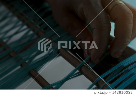 Woman hand arranging green cotton thread on traditional handloom during weaving, closeup of artisan textile production. Handmade fabric, craftsmanship, skill and cultural heritage. Traditional craft. Woman hand arranging green cotton thread on traditional handloom during weaving, closeup of artisan textile production. Handmade fabric, craftsmanship, skill and cultural heritage. Traditional craft. 142930055