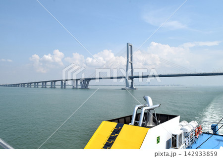 View of a bridge stretching across the sea, connecting two islands against a backdrop of beautiful blue sky and water View of a bridge stretching across the sea, connecting two islands against a backdrop of beautiful blue sky and water 142933859