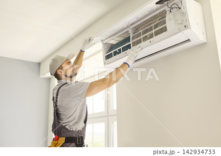 HVAC Technician Servicing Wall Mounted Air Conditioner in Bright Home Interior HVAC Technician Servicing Wall Mounted Air Conditioner in Bright Home Interior 142934733