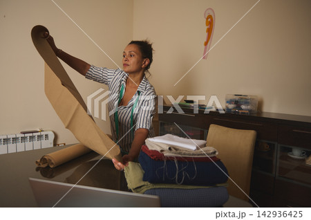 Woman preparing pattern paper and fabrics for sewing in a home studio, focused small business tailor Woman preparing pattern paper and fabrics for sewing in a home studio, focused small business tailor 142936425