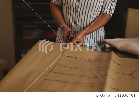 Woman cutting sewing pattern on brown paper for dressmaking project in home studio 142936461