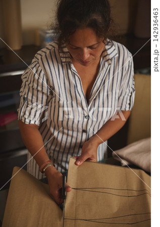 Woman cutting a sewing pattern for dressmaking at home workshop, focused craft and tailoring work 142936463