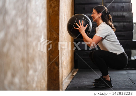 Woman performing a wall squat with a medicine ball in a gym Woman performing a wall squat with a medicine ball in a gym 142938228