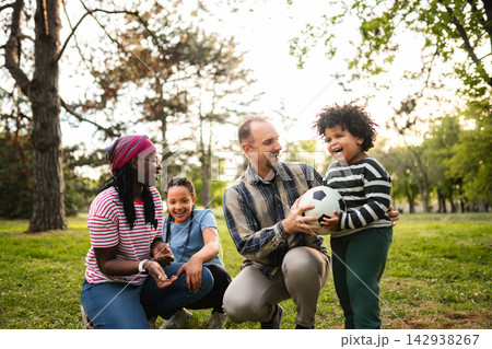 Multiethnic family enjoying afternoon playing soccer ball in park 142938267