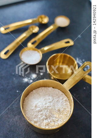 Golden measuring spoons and cup with flour, sugar, salt and yeast on dark background 142940921